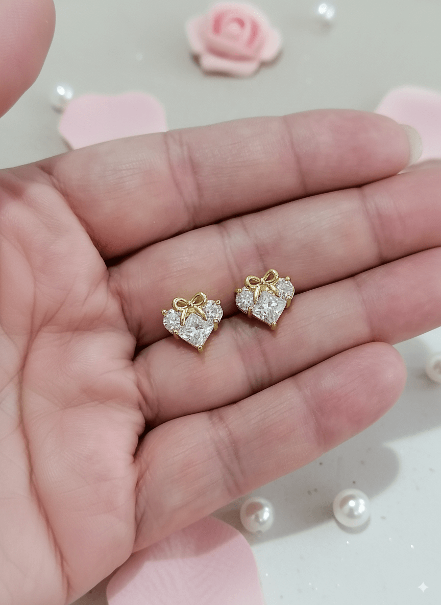Lazos de Amistad - Aretes de Rodio en forma de corazón, brillantes y con moño, sostenidos en una mano